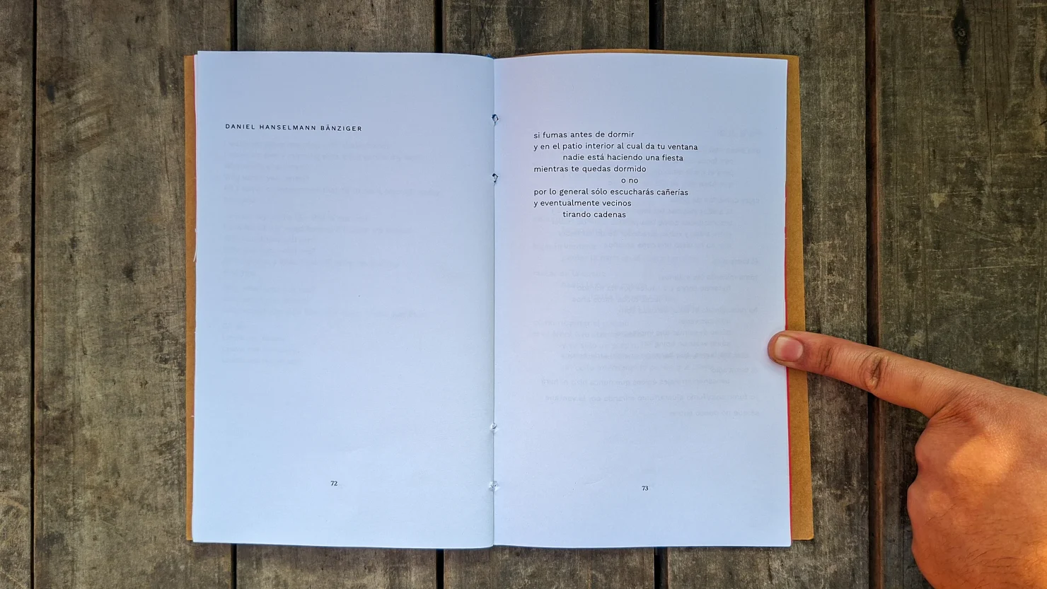 Open book at a poem by Daniel Hanselmann B&auml;nziger, a finger pointing at the page, on wooden planks